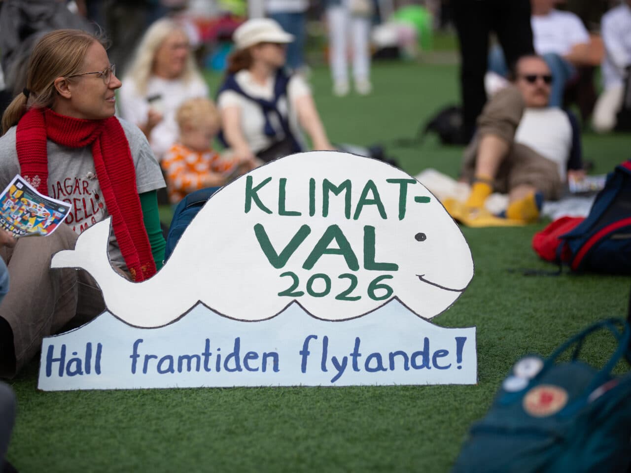 Bilden visar en grupp människor som deltar i en klimatdemonstration. I förgrunden finns en skylt ...